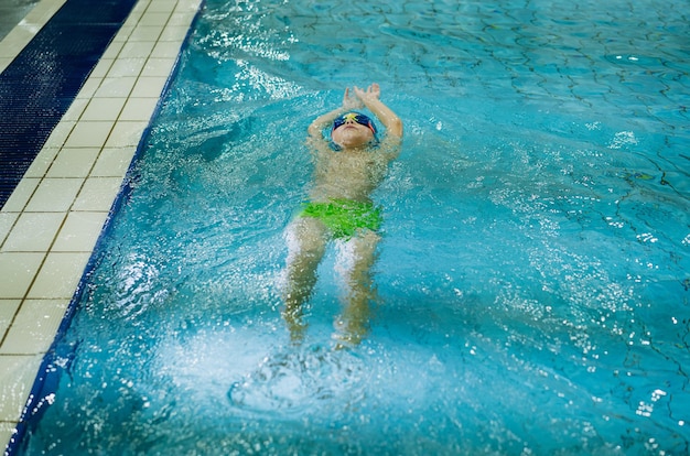 Kleine blanke jongen met een bril die de rugslag in een zwembad zwemt. hoge kwaliteit foto