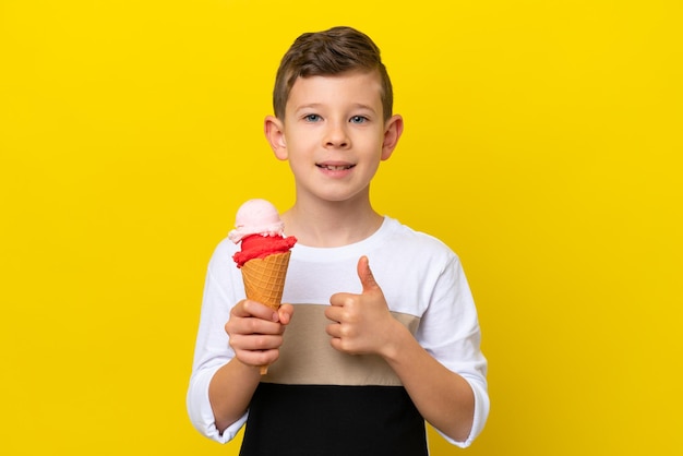 Kleine blanke jongen met een cornet-ijs geïsoleerd op een gele achtergrond met een duim omhoog gebaar