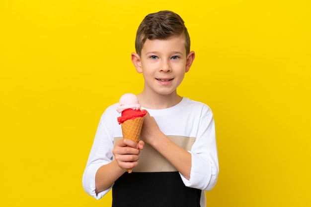 Kleine blanke jongen met een cornet-ijs geïsoleerd op gele achtergrond die een overwinning viert