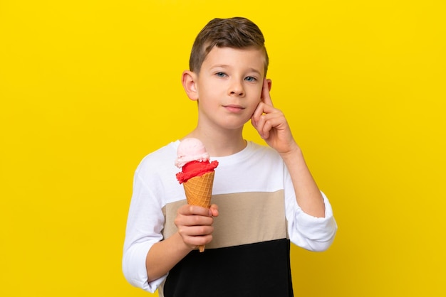 Kleine blanke jongen met een cornet-ijs geïsoleerd op gele achtergrond met twijfels en denken