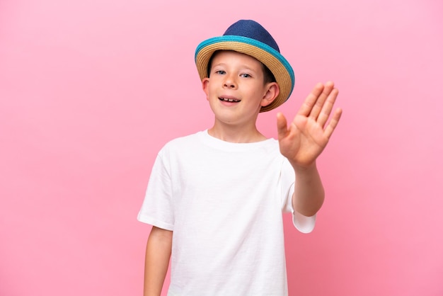 Kleine blanke jongen met een hoed geïsoleerd op een roze achtergrond die met de hand salueert met een gelukkige uitdrukking