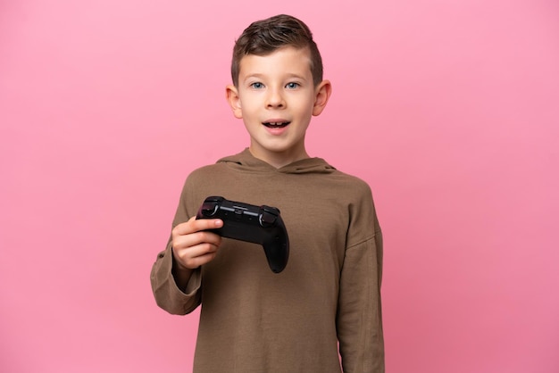 Kleine blanke jongen spelen met een video game controller geïsoleerd op roze achtergrond met verrassende gezichtsuitdrukking