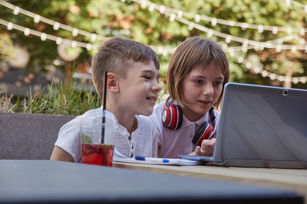 Kleine blanke schoolkinderen zitten buiten te kijken op het scherm van de laptop en hebben plezier