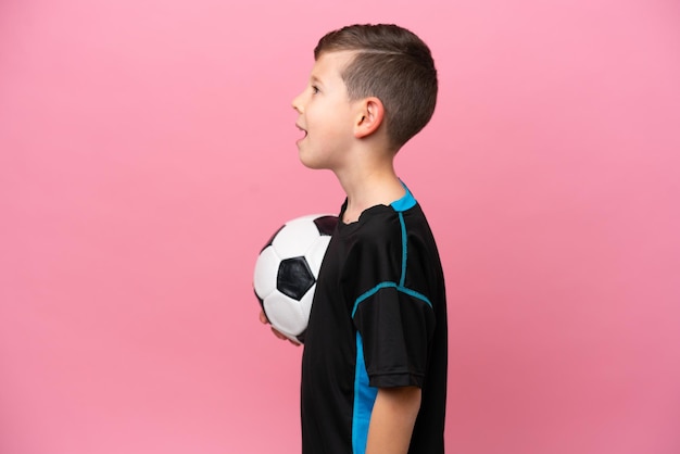 Kleine blanke voetballer jongen geïsoleerd op roze achtergrond lachend in laterale positie