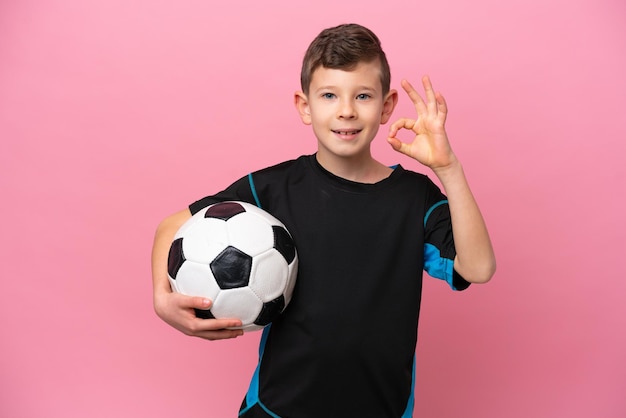 Kleine blanke voetballer jongen geïsoleerd op roze achtergrond met ok teken met vingers