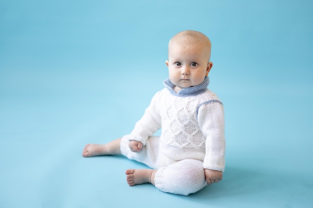 Kleine blonde babymeisje in een gebreide trui op een blauwe achtergrond isoleren, ruimte voor tekst, baby peuter in winterkleren, winter