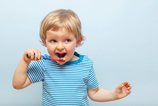 Kleine blonde jongen die zijn tanden poetst met een tandenborstel op blauwe achtergrond