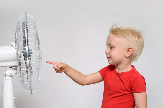 Kleine blonde jongen in een rood t-shirt raakt de ventilator met zijn vinger.