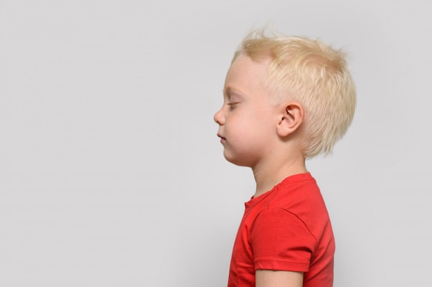 Kleine blonde jongen in rode t-shirt met gesloten ogen. Ruimte voor tekst.