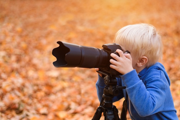 Kleine blonde jongen maakt foto's op een SLR-camera. Herfst Park