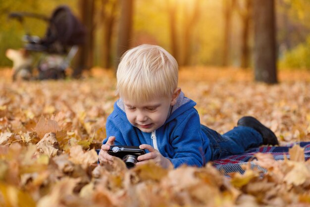 Kleine blonde jongen met camera liggend op een geruite gele herfstbladeren Herfstdag