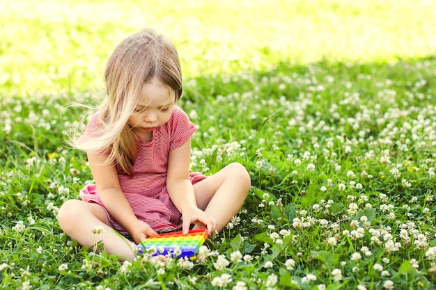 Kleine blonde jongen zittend op een groen grasveld spelen met het pop it-speelgoed. push pop bubble flexibel fidget zintuiglijk speelgoed zorgt voor ontlading