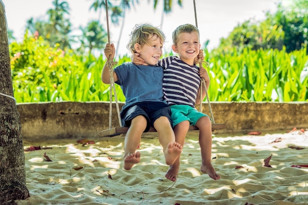 Kleine blonde jongens zittend op een schommel op een tropisch strand