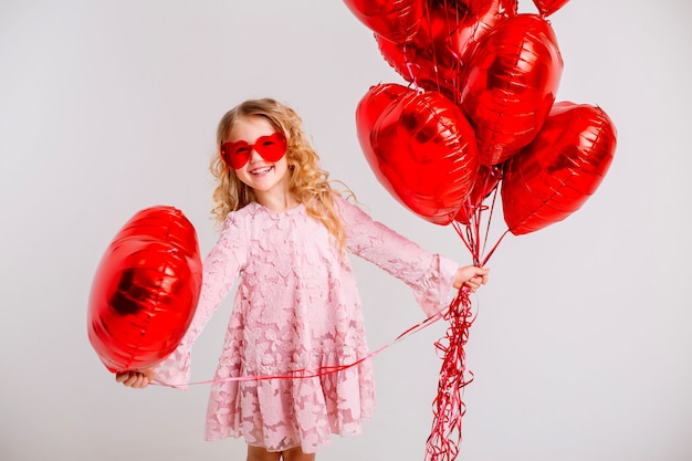 kleine blonde meisje in een roze jurk lacht en houdt veel rode hartvormige ballonnen Valentijnsdag concept