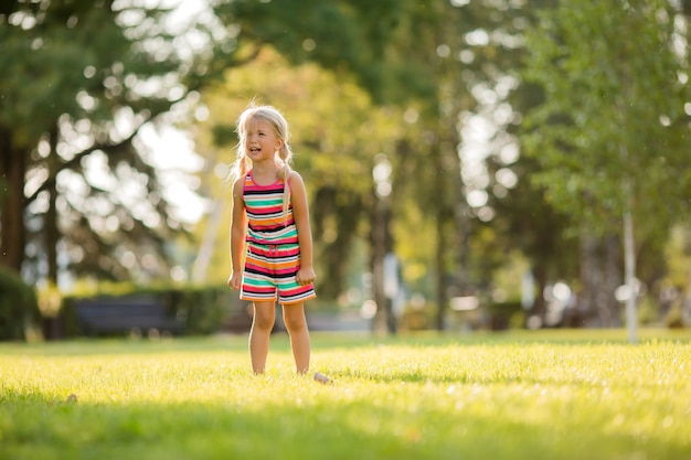 Kleine blonde meisje staat op het groene gras in de zomer en huilen