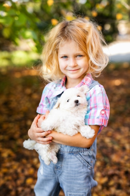 Kleine blonde peuter meisje met twee vlechten spelen met mooie witte puppy