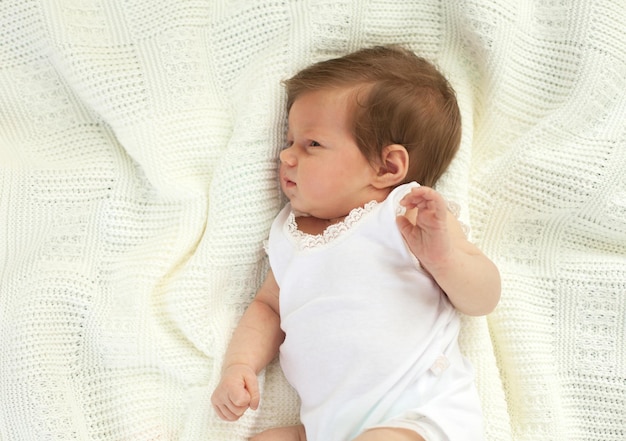 Kleine charmante baby in witte kleding liggend op de witte deken