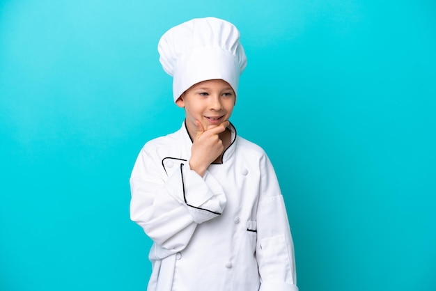 Kleine chef-kok jongen geïsoleerd op blauwe achtergrond op zoek naar de kant en glimlachen