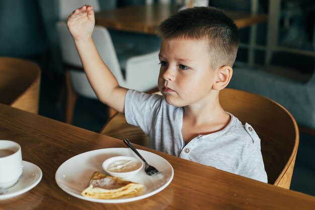 Kleine en schattige jongen ontbijten in café.