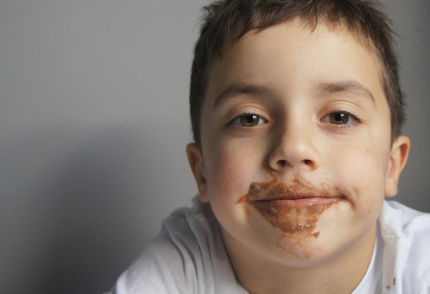 Kleine Europese jongen eet chocolade Grijze muur Schattige gelukkige jongen vallende chocolade Childhood concept