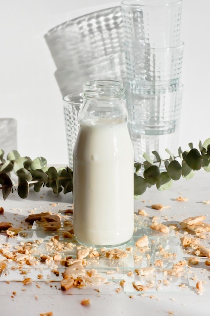 Foto kleine fles melk op doorzichtige folie en koekje kruimels met stapel glazen op de achtergrond