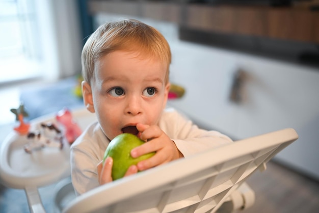 Kleine gelukkige schattige baby peuter jongen blonde zittend op de kinderstoel spelen met appel baby gezichtsbehandeling