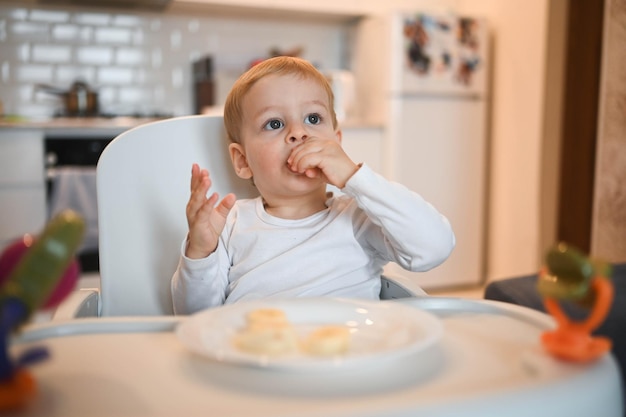 Kleine gelukkige schattige baby peuter jongen blonde zittend op de kinderstoel spelen met banaan baby gezichtsbehandeling