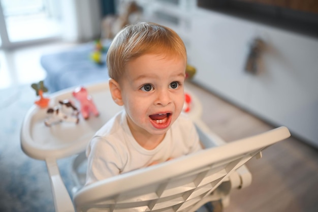 Kleine gelukkige schattige baby peuter jongen blonde zittend op een kinderstoel spelen met speelgoed baby gezichtsbehandeling