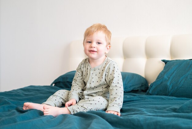 Kleine gezonde peuterjongen in groene pyjama's lachend zittend in bed thuis.