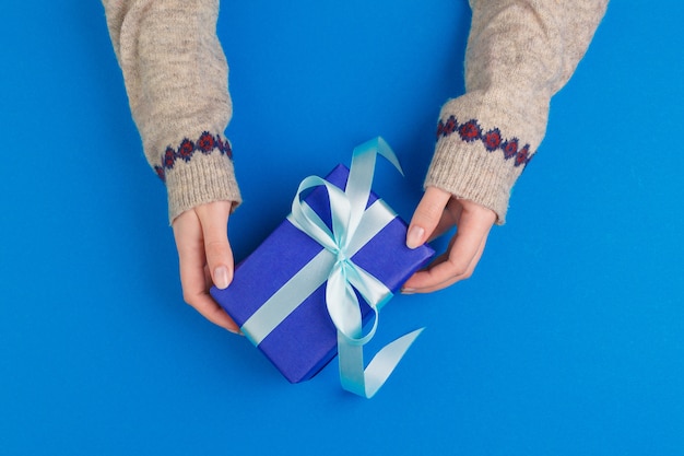 Kleine giftdoos in vrouwelijke handen op blauwe achtergrond, mening van hierboven