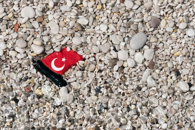 Kleine glanzende keramische Turkse vlag liggend in het grind onder water