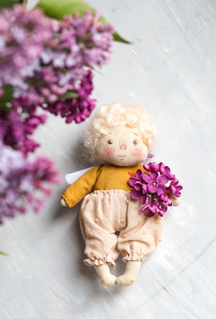 Kleine goudharige engel in de blauwe, roze, paarse, violet lila bloemen. Handgemaakt speelgoed in violet lila kleuren. Wenskaart.