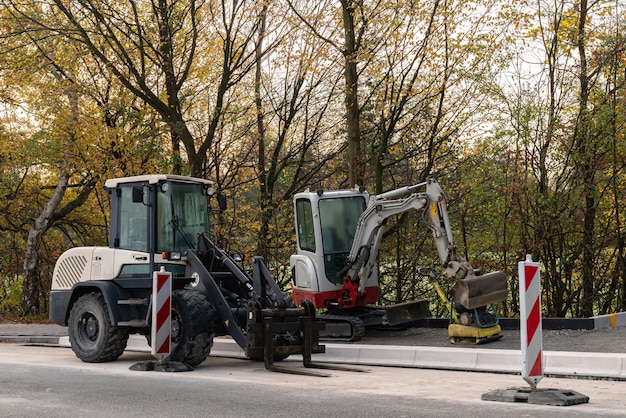 Kleine graafmachine en vorkheftruck staan aan de kant van de weg