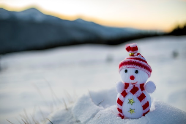 Kleine grappige speelgoed baby sneeuwpop in gebreide muts en sjaal in diepe sneeuw buiten