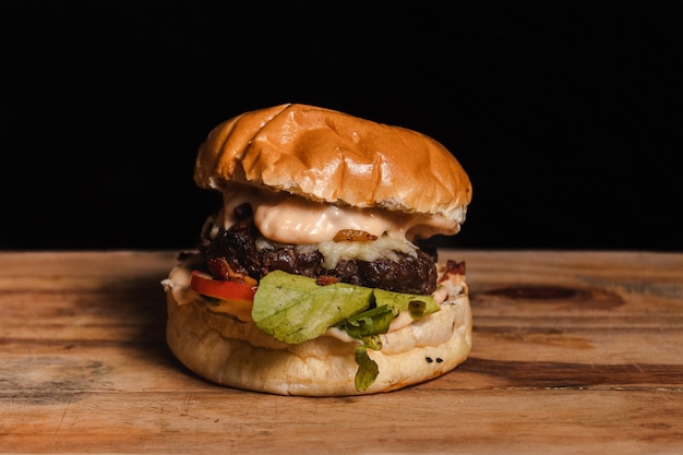 Kleine hamburger met sla en tomaat op een houten tafel met zwarte achtergrond.