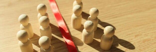 Foto kleine houten beeldjes die schaduwen werpen, gescheiden door een rood lint, op tafel bij zonlicht