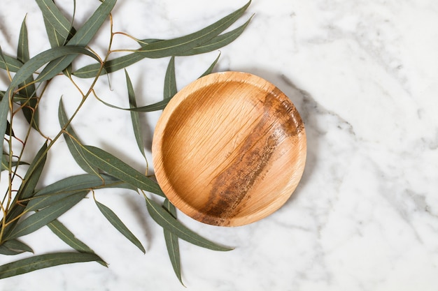 Kleine houten plaat op een marmeren tafel met eucalyptusbladeren in een bovenaanzicht