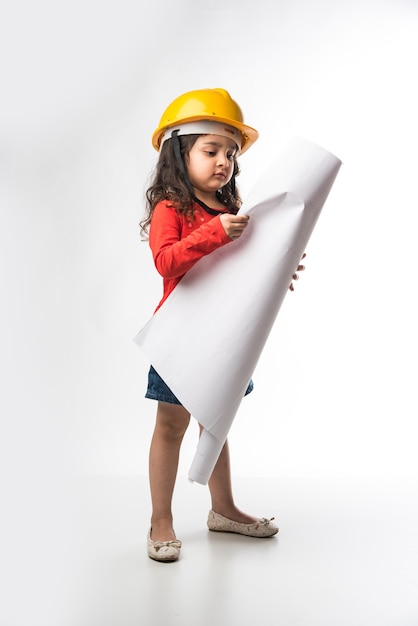 Kleine indiase meisjesingenieur met gele helm en tekenpapierrol of plan, geïsoleerd op witte achtergrond