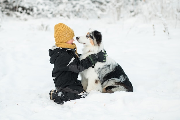 Kleine jongen Australische herder omarmen in winter woud.