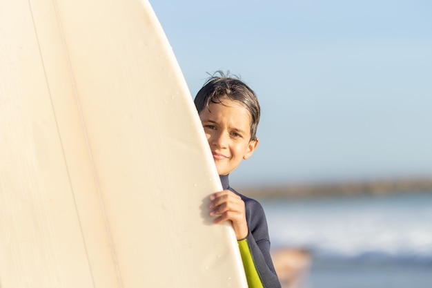 Kleine jongen die achter een surfplank vandaan gluurt