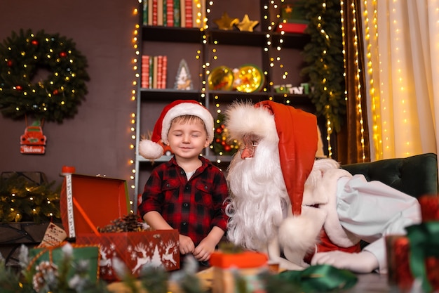 Kleine jongen die de kerstman bezoekt, doet een wens terwijl hij de ogen dicht een prettige kerstvakantie heeft