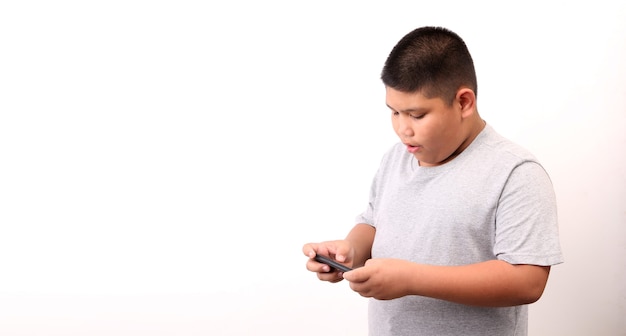Foto kleine jongen die in t-shirt slimme telefoon op witte achtergrond in studio voorstelt.