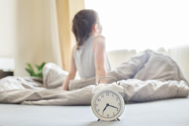 Kleine jongen die 's ochtends thuis in bed zit op een raamachtergrond met wekker