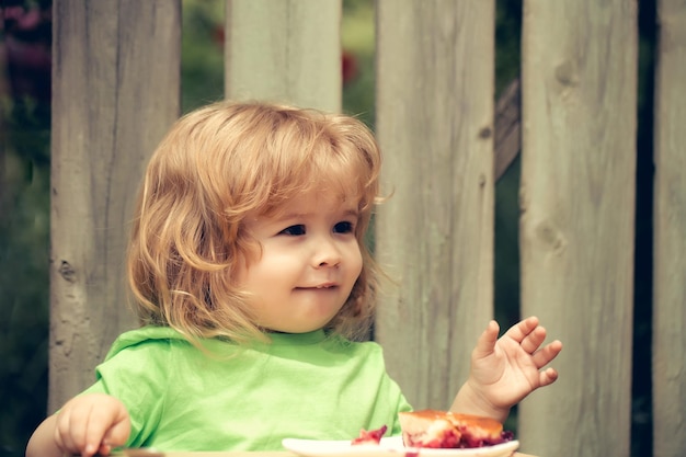 Kleine jongen die taart eet in de buurt van houten hek