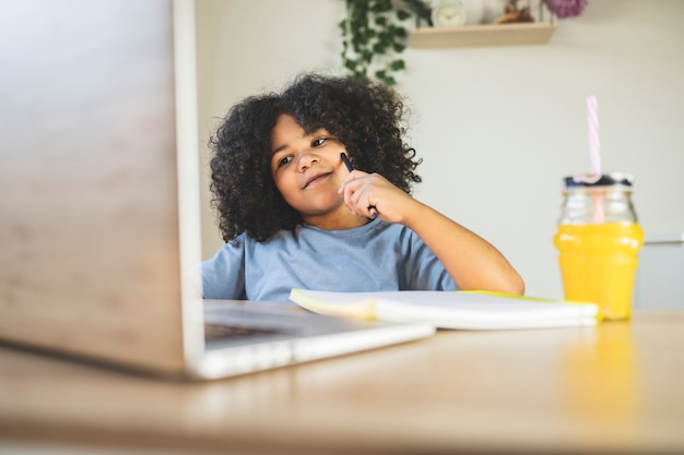 Kleine jongen doet huiswerk thuis met potlood en kijkt naar laptop