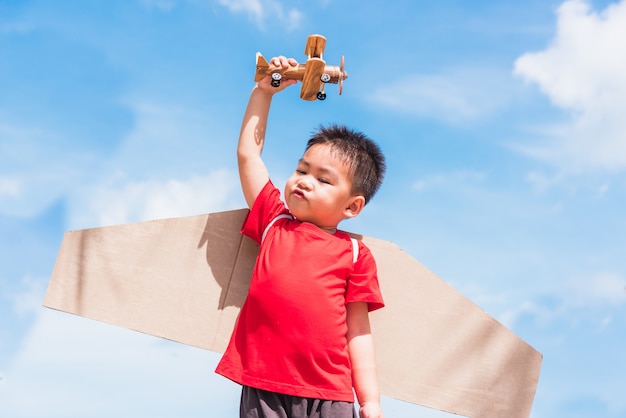 Kleine jongen draagt speelgoed vliegtuig vleugels en speelt met speelgoed vliegtuig