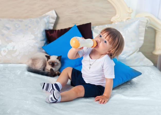 Kleine jongen drinkt melk uit de fles op het bed