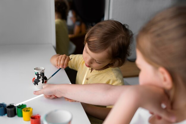 Foto kleine jongen en meisje schilderen samen vaas thuis