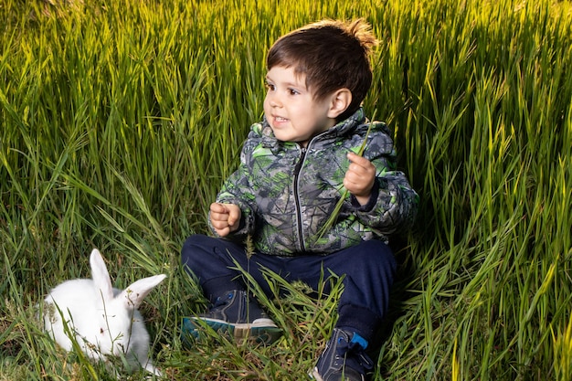 Kleine jongen en Pannon White konijn zitten op groen gras