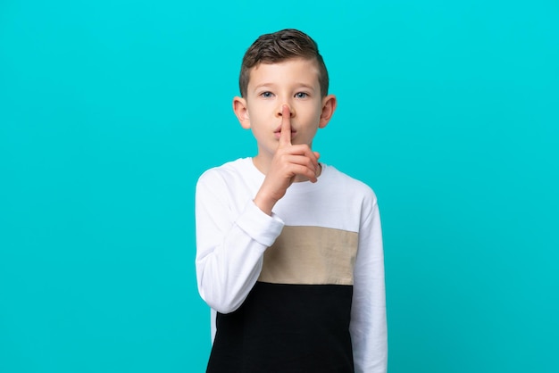 Kleine jongen geïsoleerd op een blauwe achtergrond met een teken van stilte gebaar vinger in de mond steken